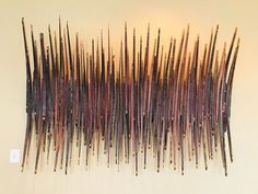 an abstract sculpture made out of sticks on a white wall in front of a light