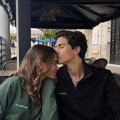 a man and woman kissing each other in front of a table at an outdoor cafe