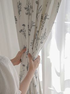 a woman is opening the curtains in front of a window with floral designs on it