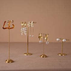 four pairs of earrings are on display in gold stands with crystal drops and pearls hanging from them