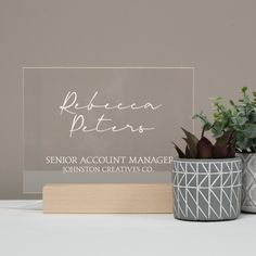 two potted plants sitting on top of a table next to a clear acrylic sign