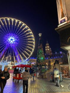 people walking around in front of a ferris wheel at night