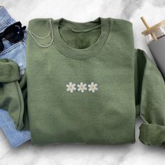 a green sweater with daisies on it next to some sunglasses and a coffee cup