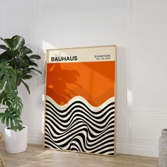 an orange and black poster sitting on top of a wooden floor next to a potted plant