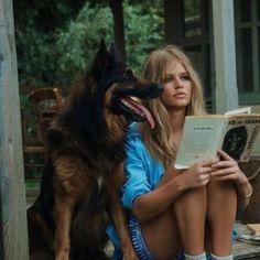 a woman is sitting on the porch with her dog and reading a book in front of her