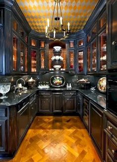 an ornate kitchen with wood floors and black cabinetry is lit by a chandelier