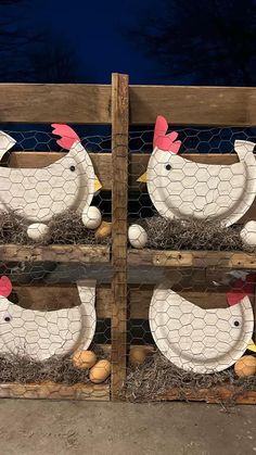 two chicken sculptures sitting on top of hay in front of a fence with chickens and eggs