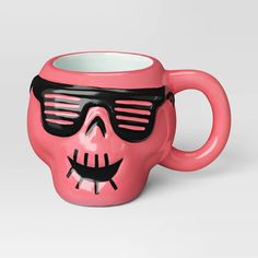 a pink coffee mug with sunglasses and a skull face on the front, sitting in front of a white background