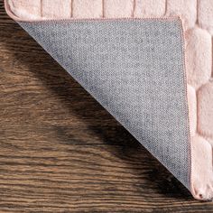 a pink and grey rug on top of a wooden floor next to a white pillow