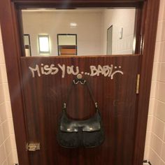 a door with graffiti written on it and a purse hanging from the handle, in front of a bathroom stall