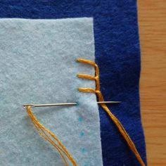 a pair of scissors and some thread on top of a piece of blue fabric with yellow needles