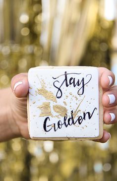 a person holding up a white and gold coaster with the words stay golden on it