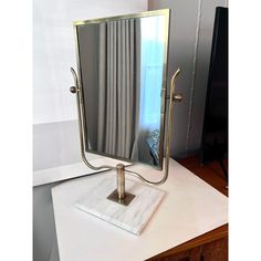 a mirror sitting on top of a white counter next to a window with drapes