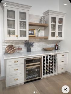 a white kitchen with marble counter tops and wine racks on the wall, along with wooden flooring