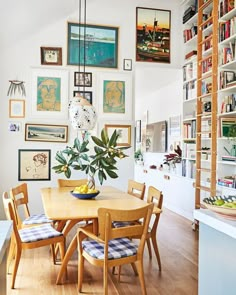 a dining room table with chairs and pictures on the wall above it, in front of a bookshelf