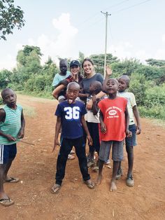 a group of people standing around each other on a dirt road with trees in the background