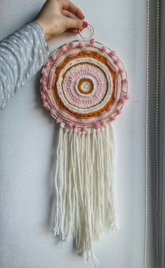 a person holding a small decorative item with fringes and beads on the bottom, in front of a white wall