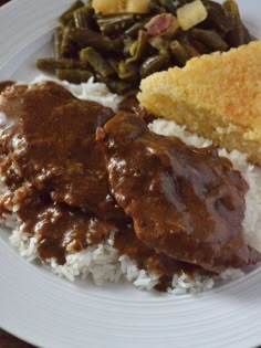 a white plate topped with meat and rice covered in gravy next to green beans