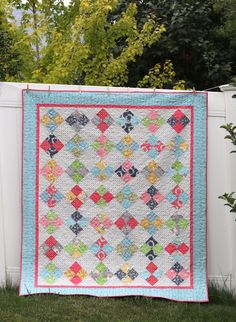 a quilt hanging on the side of a white fence with trees in the back ground