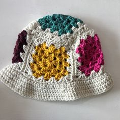 a crocheted hat with multicolored flowers on the front and sides, sitting on a white surface