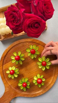 someone is decorating some flowers on a wooden platter with red roses in the background