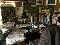 a cluttered desk with lots of books and pictures on the wall in front of it