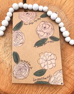 a brown card with white flowers and green leaves on it next to some beaded bracelets