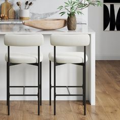 two white bar stools sitting on top of a wooden floor next to a counter