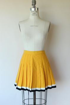 Charming 1960s cheerleader mini skirt in yellow with black and white stripes at the bottom.  Has a button and metal zipper at the waist. Unlined.  Looks and feels like wool to me. Label reads: none.  Small size I'd say. Excellent to near mint vintage condition. The only thing to note is perhaps a bit of very faint graying around the waist. Measurements when lying flat and pulled taut. Doubled at waist and hip. Waist: 25" Hips: free  Waist to bottom hem: 16.5" Please note: These are vintage, preworn and/or preloved items. I do my best to list any issues, but signs of wear should be expected. Please feel free to contact me with any questions. I'm truly happy to help in any way possible and I'm always up for a chat. Any accessories shown, including crinolines, are for display only, not includ 1960s Mini Skirt, Black Cheerleaders, Retro Looks, Pom Pom Girl, Robes Vintage, Yellow Skirt, Yellow And Black, Metal Zipper, Vintage 1960s