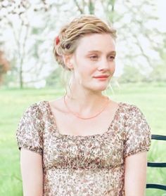 a woman sitting on a park bench wearing a dress and holding a cell phone in her hand