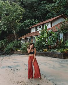 a woman standing on top of a sandy beach next to a lush green forest covered hillside