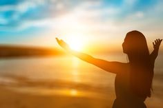 a woman is standing on the beach with her arms outstretched in front of the sun