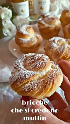 a hand holding a pastry in front of several other pastries on a white tablecloth