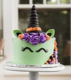 a green cake decorated with purple flowers and a black horn on top is sitting on a silver platter