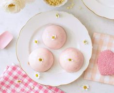 three pink donuts on a white plate next to flowers and napkins with gold accents