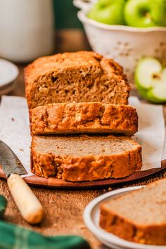 sliced loaf of banana bread sitting on top of a wooden cutting board next to green apples