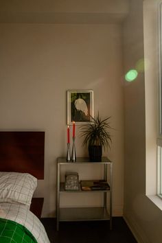 a bedroom with a bed, nightstand and plant on the shelf next to the window