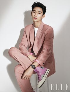 a man in a pink suit and sneakers sitting on a white wall with his legs crossed