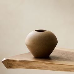 a brown vase sitting on top of a wooden table next to a white wall in the background