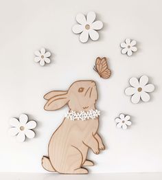 a wooden cutout of a rabbit with flowers and a butterfly in the air, on a white background