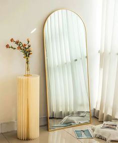 a tall mirror sitting on top of a floor next to a vase filled with flowers