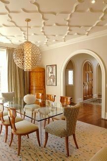 an elegant dining room with glass table and beige upholstered chairs, chandelier, arched doorway leading to the living room