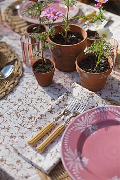 the table is set with pink plates, silverware and flowers in small potted plants