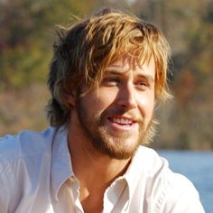 a man with blonde hair and beard wearing a white shirt sitting in front of water