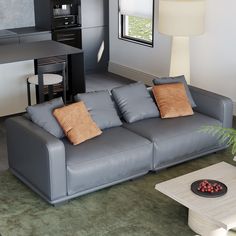 a grey couch with two pillows on it in front of a coffee table and window