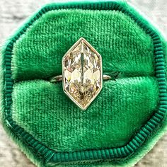 a ring that is sitting on top of a green velvet case with a diamond in the center