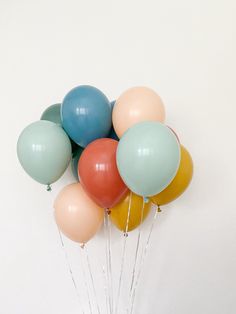 a bunch of balloons floating in the air on top of a white wall with string