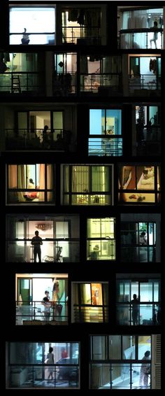 people are standing in the windows of an apartment building at night