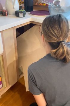 a woman sitting in front of a kitchen counter with an open drawer on the side