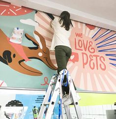 a woman standing on a ladder painting a mural